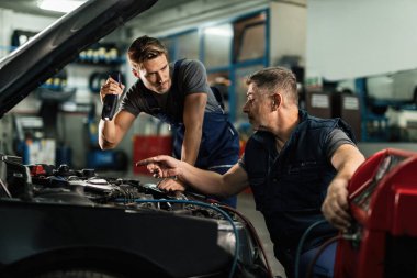 Auto mechanics communicating while doing diagnostic of air conditioning system in a workshop. 