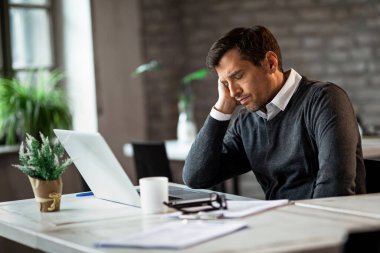 Exhausted businessman resting with eyes closed at his office desk while feeling tired of work. 
