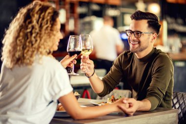 Loving couple celebrating and toasting with glass of wine while holding hands in a restaurant. 