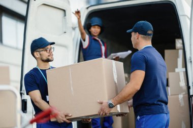 Delivery men cooperating while loading cardboard boxes in a mini van. Their female colleagues is gesturing from a van. 