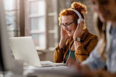 Happy freelance worker having fun while working on laptop and listening music over headphones in the office. 