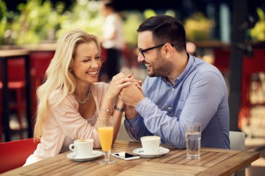 Cheerful couple holding hands and flirting while being on a date in a cafe. 