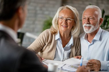 Happy mature couple talking to their real estate agent while going through paperwork on a meeting in the office. 