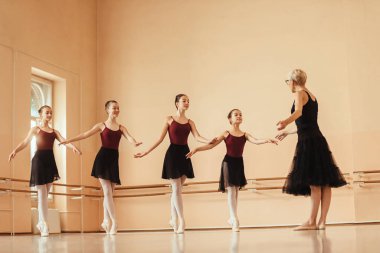 Full length of ballet teacher holding a dance class to group of ballerinas.