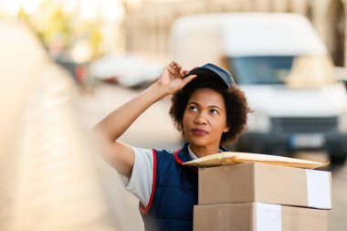 Black female courier carrying packages and looking for delivery address in the city. 