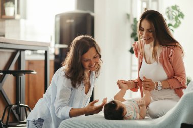 Young female couple enjoying while playing with their baby daughter at home. 