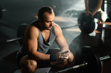 Young bodybuilder preparing for a deadlift and clapping his hands with sports chalk in a gym. 