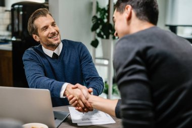 Happy insurance agent shaking hands with his client after the consultations. 