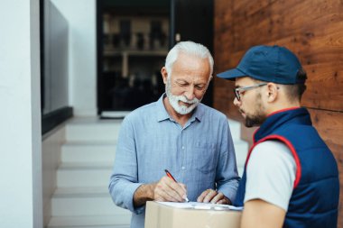 Smiling senior man receiving home delivery and signing to a deliverer. 