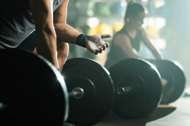 Unrecognizable muscular build man preparing his hands with talcum powder on weight training in health club. Focus is on hand.