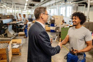 Happy black manual worker shaking hands with company engineer in at  factory plant. 