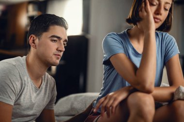 Pensive man thinking of problems he has in a relationship with his girlfriend while she is sitting next to him at home. 