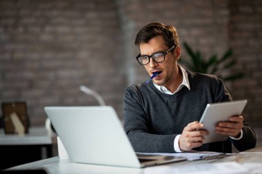 Dedicated businessman using laptop and digital tablet while working in the office. 