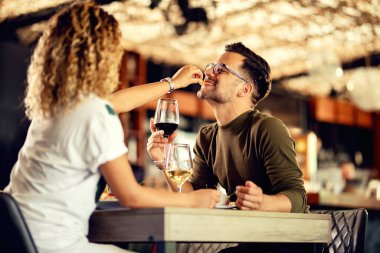 Happy man drinking wine and having fun while girlfriend is sharing her food with him. 