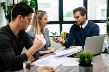 Happy real estate agent showing to young couple a mortgage contract on a meeting in the office. 