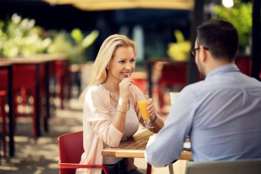 Happy woman talking to her boyfriend while drinking juice on a date in a cafe. 
