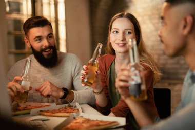 Young freelancers communicating while eating pizza and drinking beer on a break in the office. 
