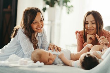 Smiling mothers playing with their babies and enjoying in motherhood at home. 