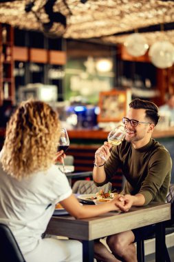 Happy couple having fun and drinking wine while holding hands in a restaurant.