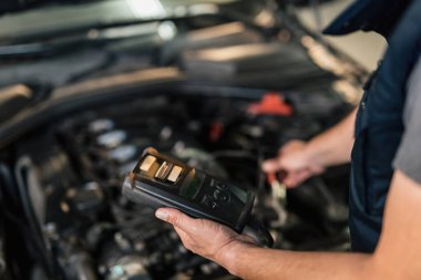 Close-up of mechanic using diagnostic tool while checking engine performance in auto repair shop. 