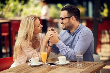 Smiling couple holding hands and flirting while having a date in a cafe. 