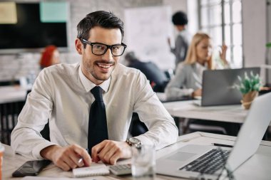 Portrait of happy businessman working at his desk in the office and looking at camera. 