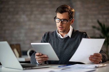 Businessman multi-tasking while using wireless technology and working on paperwork in the office. 