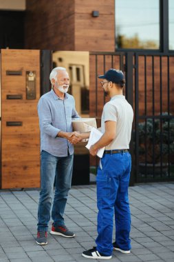 Senior man feeling satisfied with home delivery and handshaking with a courier in front of his house. 