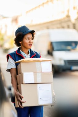Black female courier carrying packages while making delivery in the city. 