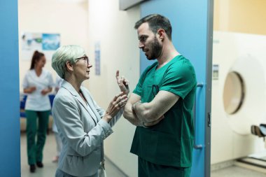 Mature woman talking to a surgeon while standing in a hallway in the hospital. 