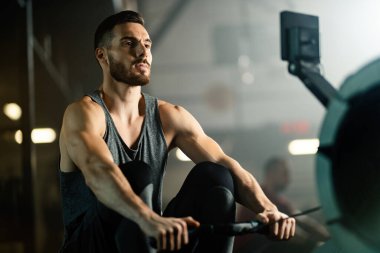 Young male athlete exercising on rowing machine while working out in health club. 