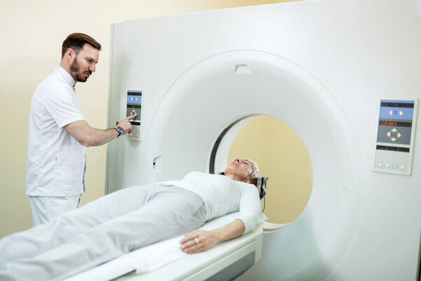 Medical technician starting MRI scan procedure of mature patient at clinic. 