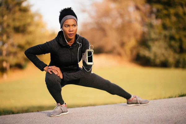African American athletic woman doing stretching exercise during sports training in the park. 