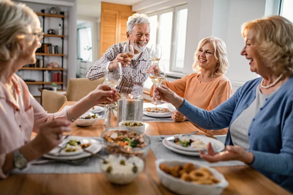 Group of mature people toasting with wine and having fun while gathering on a lunch at home.