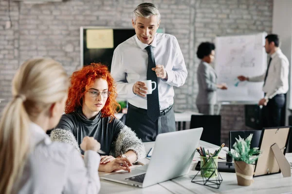 Young businesswoman using computer while having a meeting with colleagues in the office. There are people in the background. 