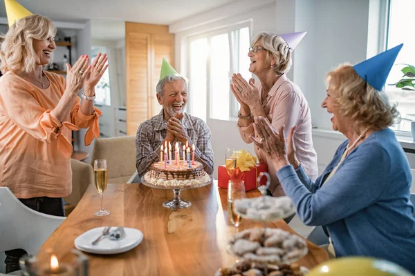 Happy mature women clapping hands and surprising their friend with a birthday cake at home.