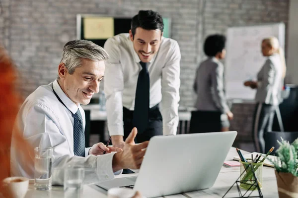 Two happy businessmen reading an e-mail on laptop in the office. Focus is on mid adult businessman. 