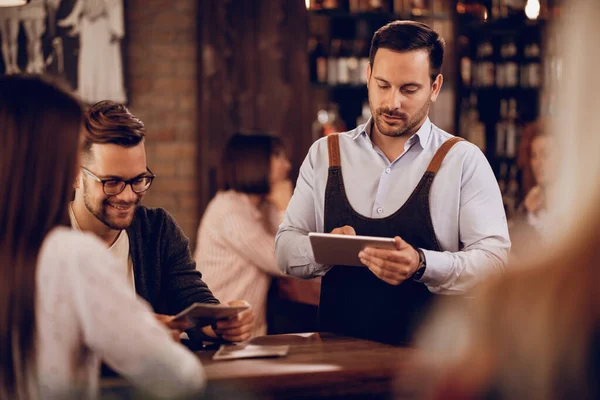 Young Waiter Writing Order Touchpad While Serving Guests Bar — Stockfoto