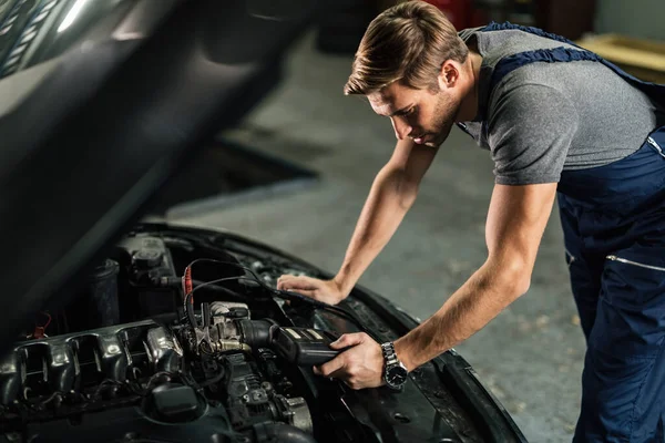 Auto mechanic doing car battery check while using diagnostic tool in a service workshop.