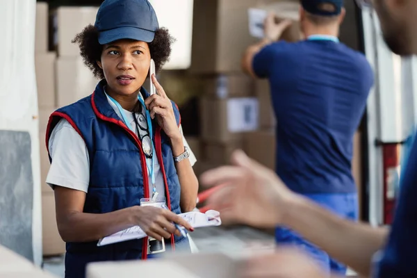 Black Female Deliverer Communicating Coworker While Talking Mobile Phone Organizing — Stock Fotó