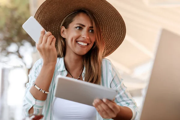 Multi-tasking woman feeling confused while using mobile phone, touchpad and laptop in a cafe.