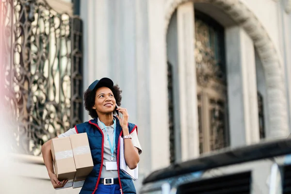 Happy African American Delivery Woman Carrying Packages Talking Mobile Phone — Zdjęcie stockowe