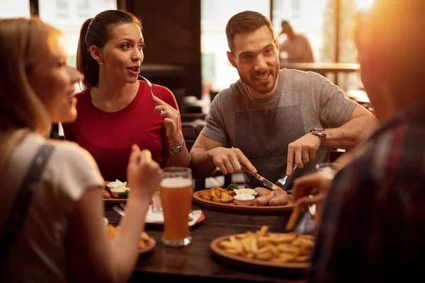 Young happy people eating in a pub and talking to each other.