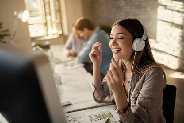 Ofiste bilgisayar başında çalışırken kulaklık takan mutlu bir iş kadını. İş arkadaşları arka planda.. 