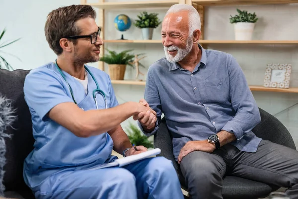 Happy senior man shaking hands with a doctor who is being in a home visit.