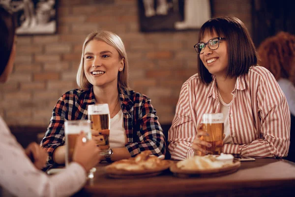Happy women communicating while drinking beer and relaxing in a tavern. 