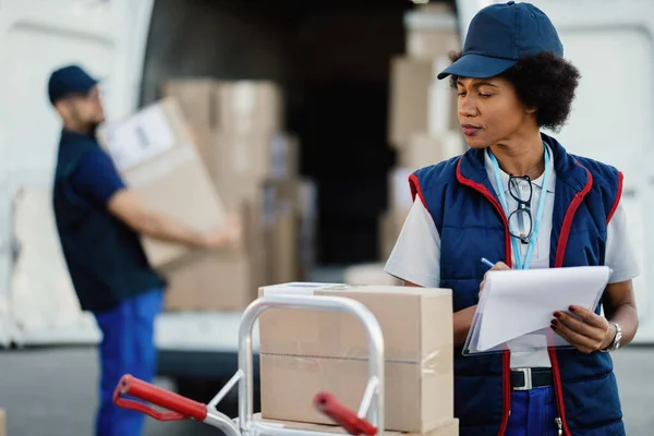 Black Female Delivery Woman Taking Notes Clipboard While Her Coworker — Foto Stock