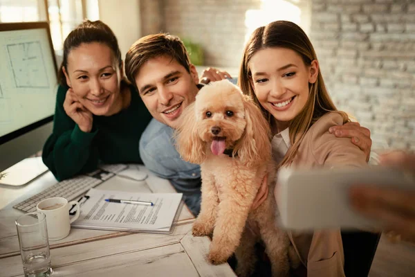 Team of creative business people taking selfie with their poodle in the office.