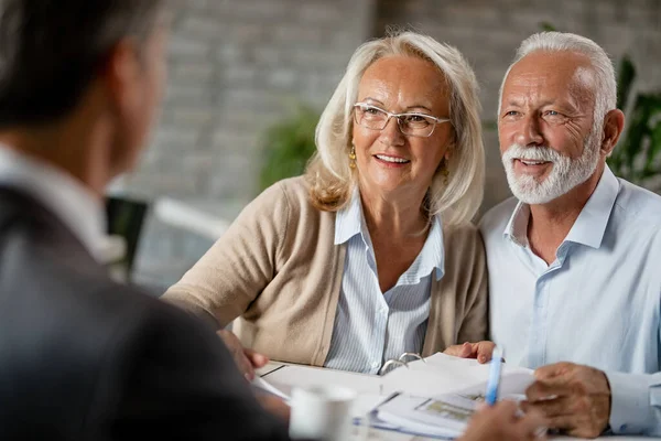 Happy mature couple talking to their real estate agent while going through paperwork on a meeting in the office. 
