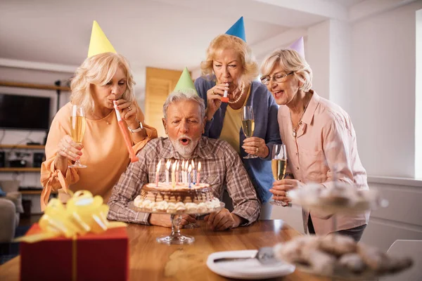 Mature man celebrating Birthday with his friends and blowing candles on a cake at home.